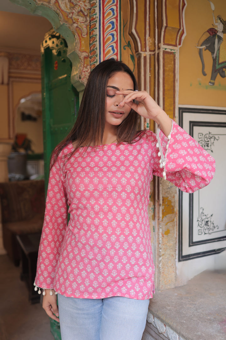 Woman wearing a pink floral top in an indoor setting with decorative walls.